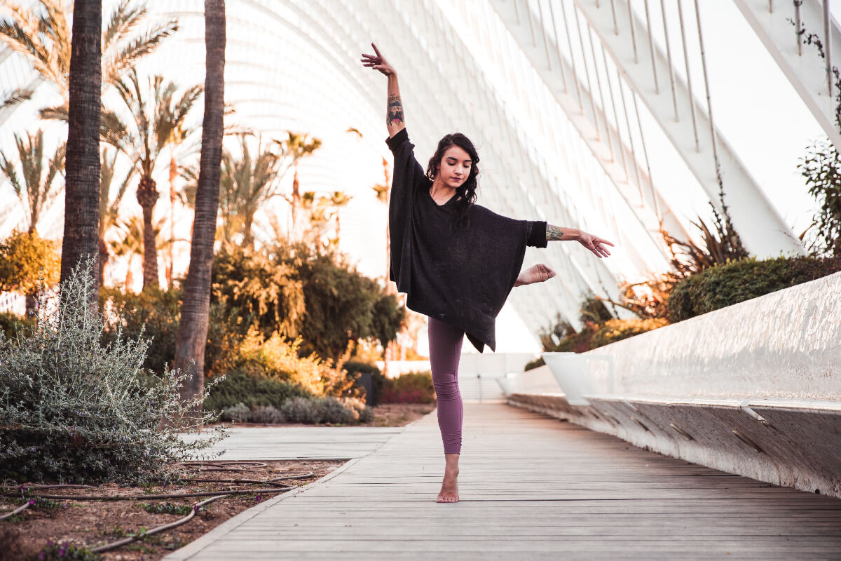 Person practicing yoga on a wooden path with palm trees and a modern bridge in the background
